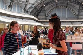 Meet-the-author at a book table: an author talks with a visitor; a large fair hall with people in the background.