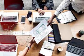 Two people hand a piece of paper over a desk full of laptops