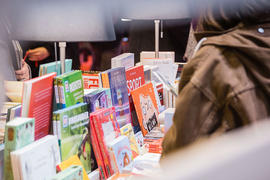 Eine Frau stöbert durch die Titel auf einem Bücherstapel.