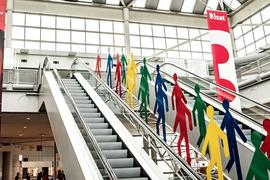 Große Plakate hängen von der Decke herab an einer Rolltreppe