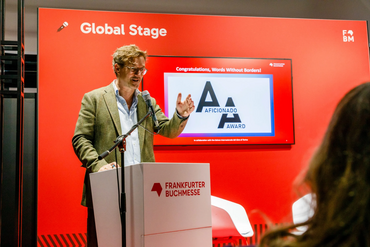 Speech on the Global Stage: a speaker gestures at the lectern in front of the Aficionado Award logo.