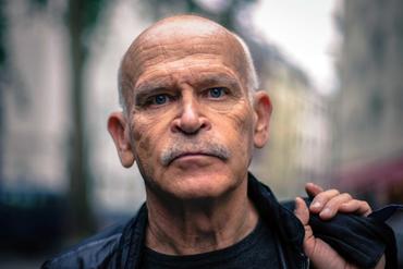 Porträt des Journalisten und Autors Günter Wallraff. Er schaut frontal in die Kamera und hält, über seine Schulter geschlungen, eine Tasche mit der Hand fest.