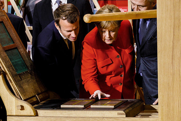 Merkel und Macron bedienen die Druckmaschine 