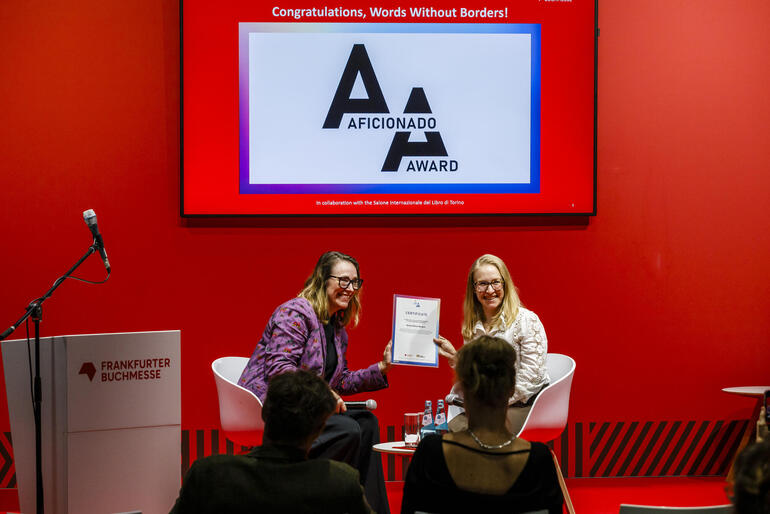 The 2026 Aficionado Award ceremony at the Frankfurt Book Fair. Two smiling women are holding the winner’s certificate.