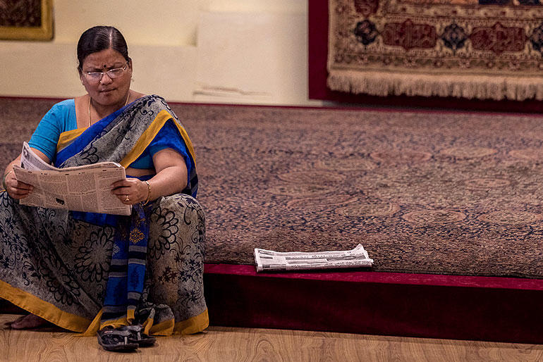 A woman sits on a carpet and reads in the paper