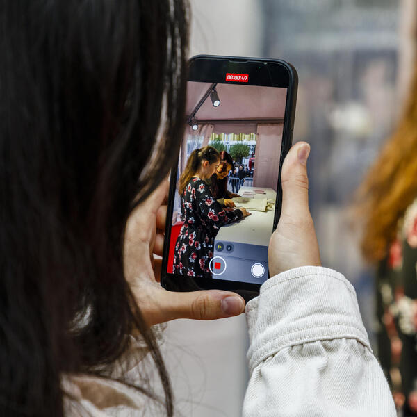 Blick auf einen Smartphone-Bildschirm, der gerade eine Autorin beim Signieren filmt. 