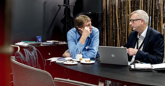 Two Men talk in front of a Computer