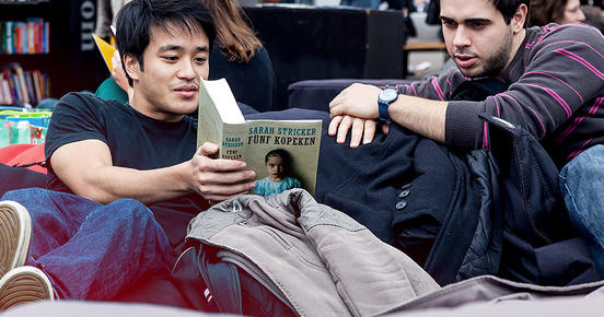 Zwei Studenten sitzen auf der Agora und lesen zusammen ein Buch