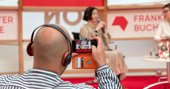 Ein Mann filmt mit seinem Smartphone ein Bühnengespräch mit Sayaka Murata.