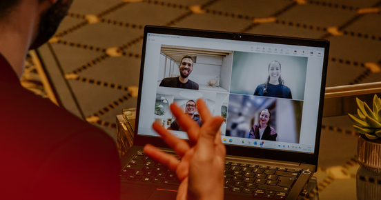 Person nimmt an einem Video-Call am Laptop teil; vier Teilnehmende sind im Raster auf dem Bildschirm zu sehen.