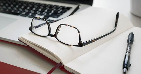 Eine Brille und ein Notizbuch liegen auf einem Laptop
