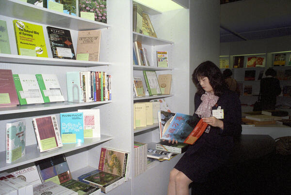 A hostess flips through a book at a stand with Asian titles