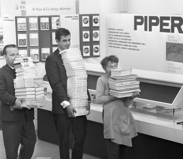 Mitarbeiter tragen am 08.10.1963 vor der Eröffnungsveranstaltung der Buchmesse Bücherstapel durch die Messehalle.