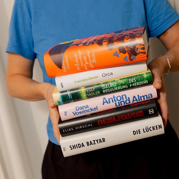 Eine Person hält einen Stapel mit den Büchern der Shortlist für den Deutschen Buchpreis 2026