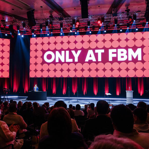 Ein großer Veranstaltungssaal mit Publikum und Bühne, auf einer Leinwand die Aufschrift "Only at FBM"