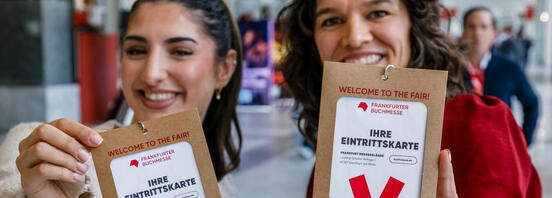 Zwei Frauen halten freudig ihre Eintrittskarten für die Frankfurter Buchmesse in die Kamera.