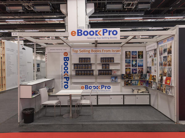 Foto von einem Messestand mit Tisch und Stühlen im Vordergrund und Bücherregalen im Hintergrund