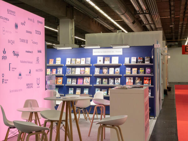 Foto von einem Messestand mit beleuchteter Wand, Stehtischen und Barhockern.