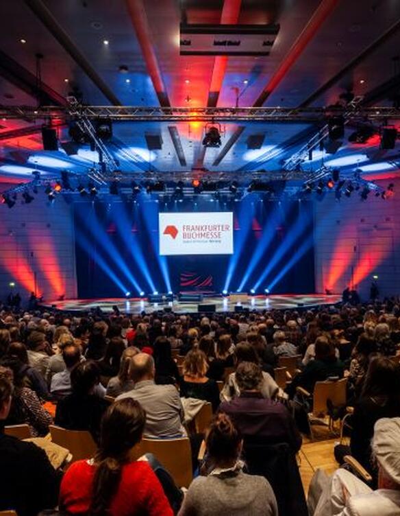 Blick auf eine Bühne in einem großen Saal mit Frankfurter Buchmesse Logo und viel Publikum.