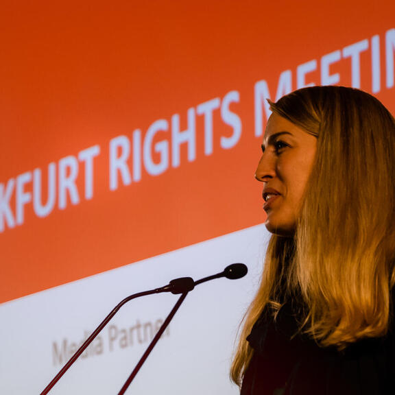 Sprecherin steht vor zwei Mikrofonen. 