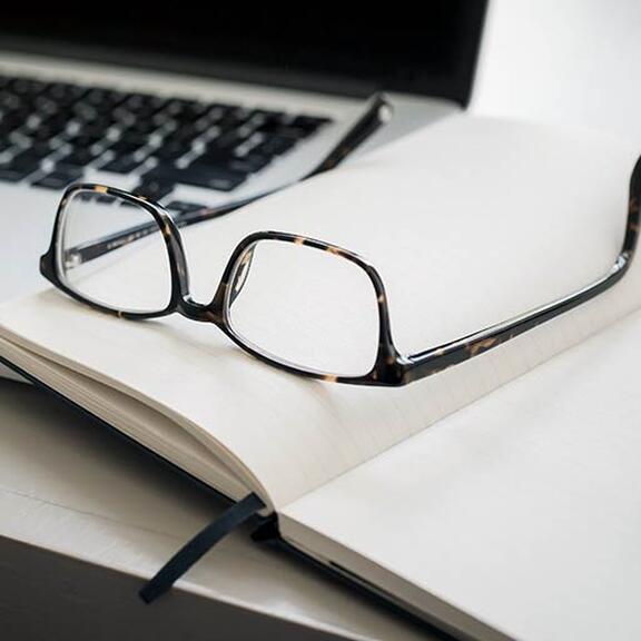 Eine Brille und ein Notizbuch liegen auf einem Laptop