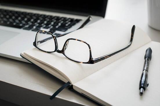 Eine Brille und ein Notizbuch liegen auf einem Laptop