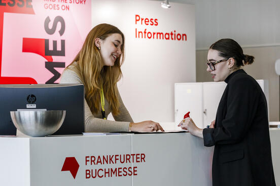 Staff and media representative talk at the info desk at Frankfurter Buchmesse's Press Centre 