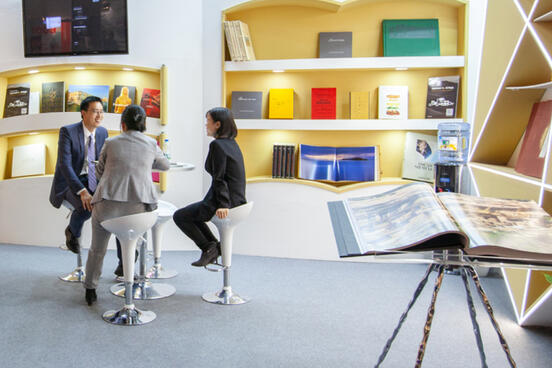 Drei Menschen sitzen auf Barhockern an einem Messestand mit Büchern (dekorativ)