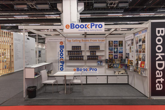 Fair stand in a fair hall with books on wall shelves and a table with two chairs. 