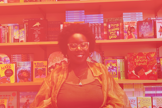 Porträt von Ama Badu, die vor einem Bücherregal steht, das mit Kinder- und Jugendbüchern gefüllt ist.