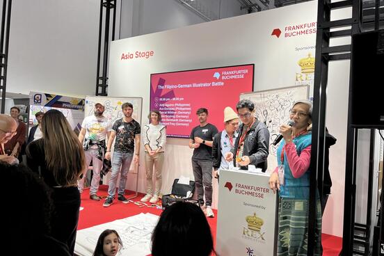 Eine Gruppe von Menschen steht auf einer Messebühne, die die Aufschrift "Asia Stage" trägt.