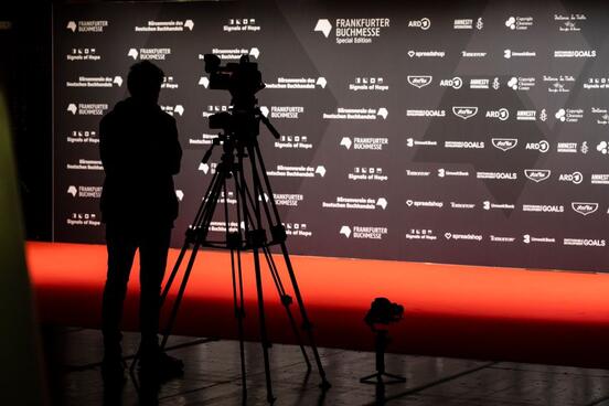 Ein Medienvertreter steht mit seiner Kamera vor der Pressewand der Eröffnungsfeier. 