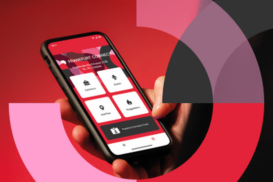 Eine Hand hält ein Smartphone in der Hand, auf dem die Startseite der App zu sehen ist. 