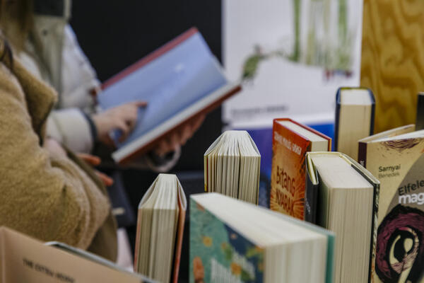 Person blättert in einem Buch; im Vordergrund stehen mehrere Bücher auf einem Tisch.