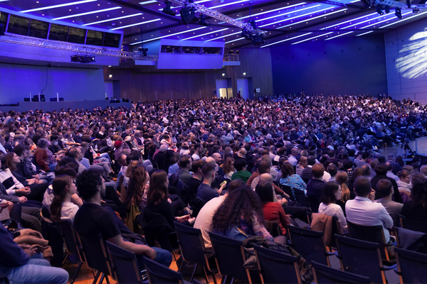 Photo of a big audience looking at a stage. 