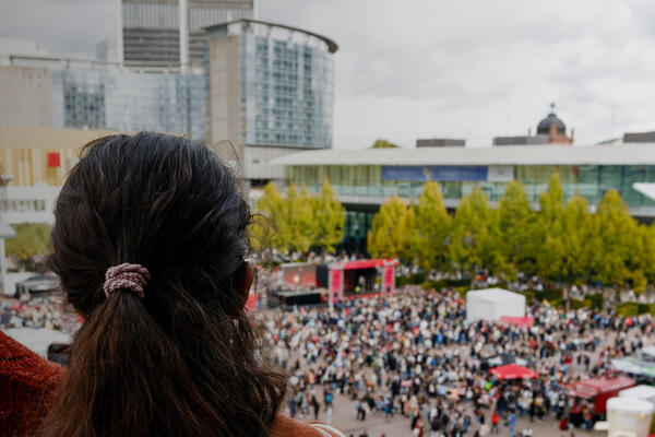Two persons are overlooking the plaza filled with people within the fair grounds.