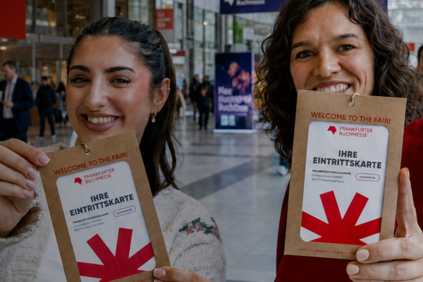 Zwei Personen in einer Messehalle halten lächelnd Tickets für die „Frankfurter Buchmesse“ in die Kamera.